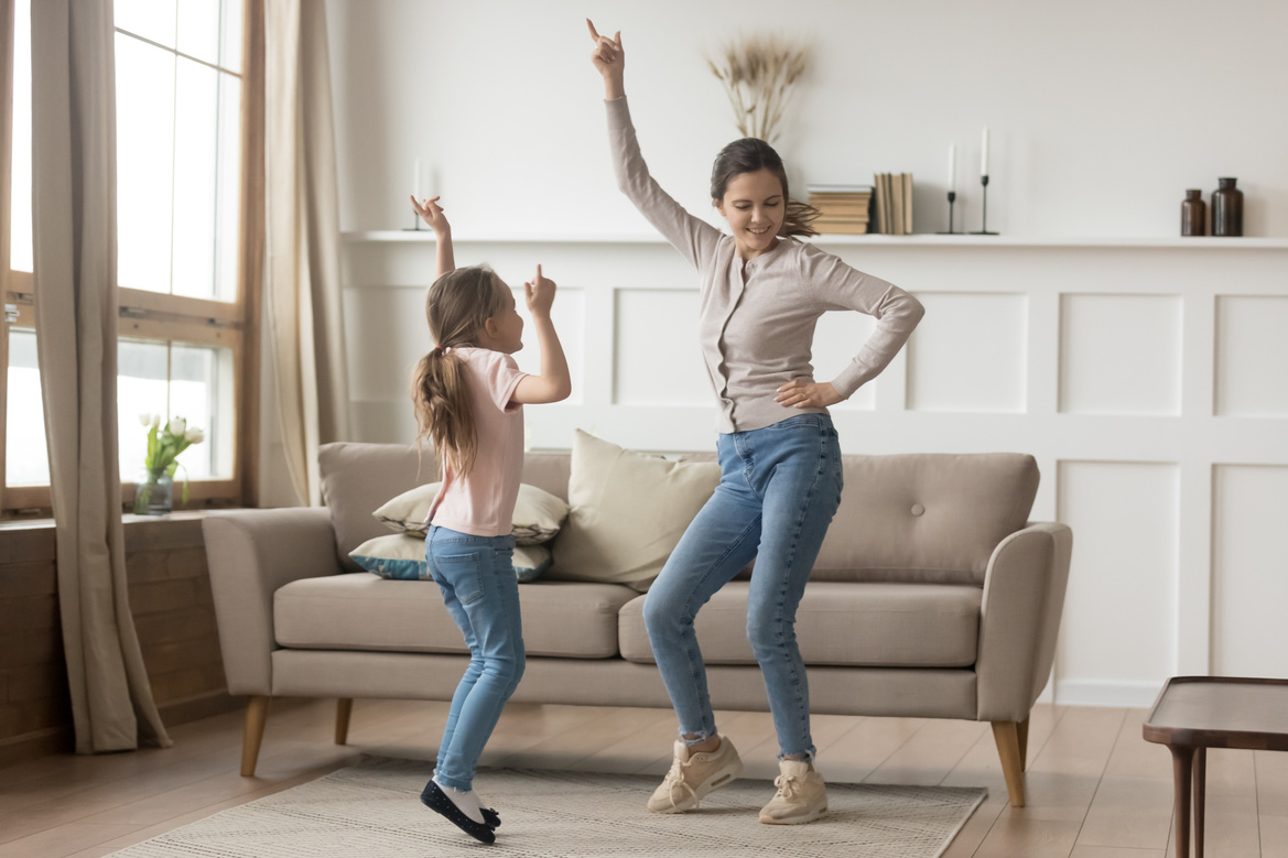Active mother dancing at home with little daughter